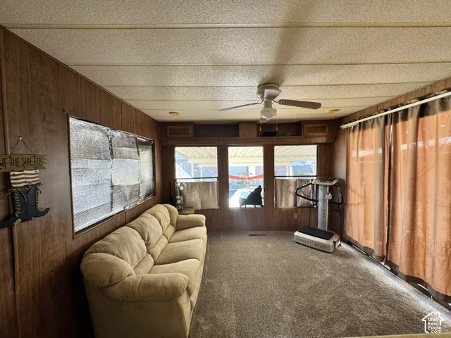 Wood-paneled interior space featuring integrated overhead storage cabinets, a ceiling fan with light fixture, and large multi-pane windows