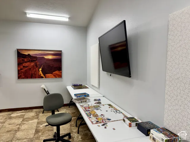 Neutral-toned interior space featuring light-colored wall surfaces, stone-finish tile flooring, and a wall-mounted electronic display