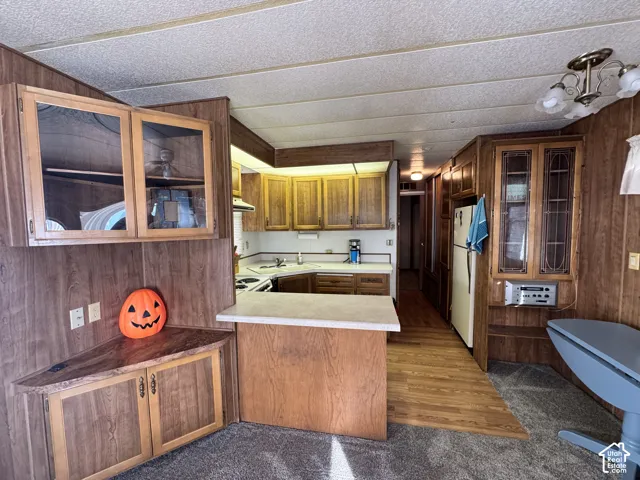 Kitchen featuring wood cabinetry, integrated glass-front display storage, a peninsula with a solid-surface countertop, and wood-finish flooring