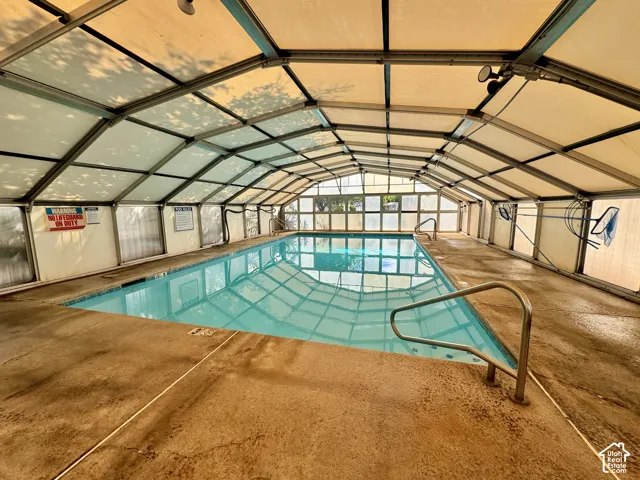 Enclosed indoor swimming pool featuring a retractable arched structure, concrete deck, and metal handrails