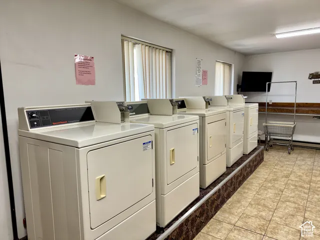 Laundry facility featuring multiple industrial-grade clothes dryers, elevated platform flooring, tile flooring, and a wooden built-in folding counter