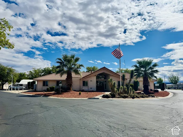 Single-story exterior featuring a light-toned stucco facade, a neutral-toned tile roof, an arched entryway, and desert landscaping with palm trees