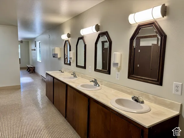Extended vanity featuring four undermount sinks, solid-surface countertop, wood-finish cabinetry, individual framed mirrors, and wall-mounted lighting