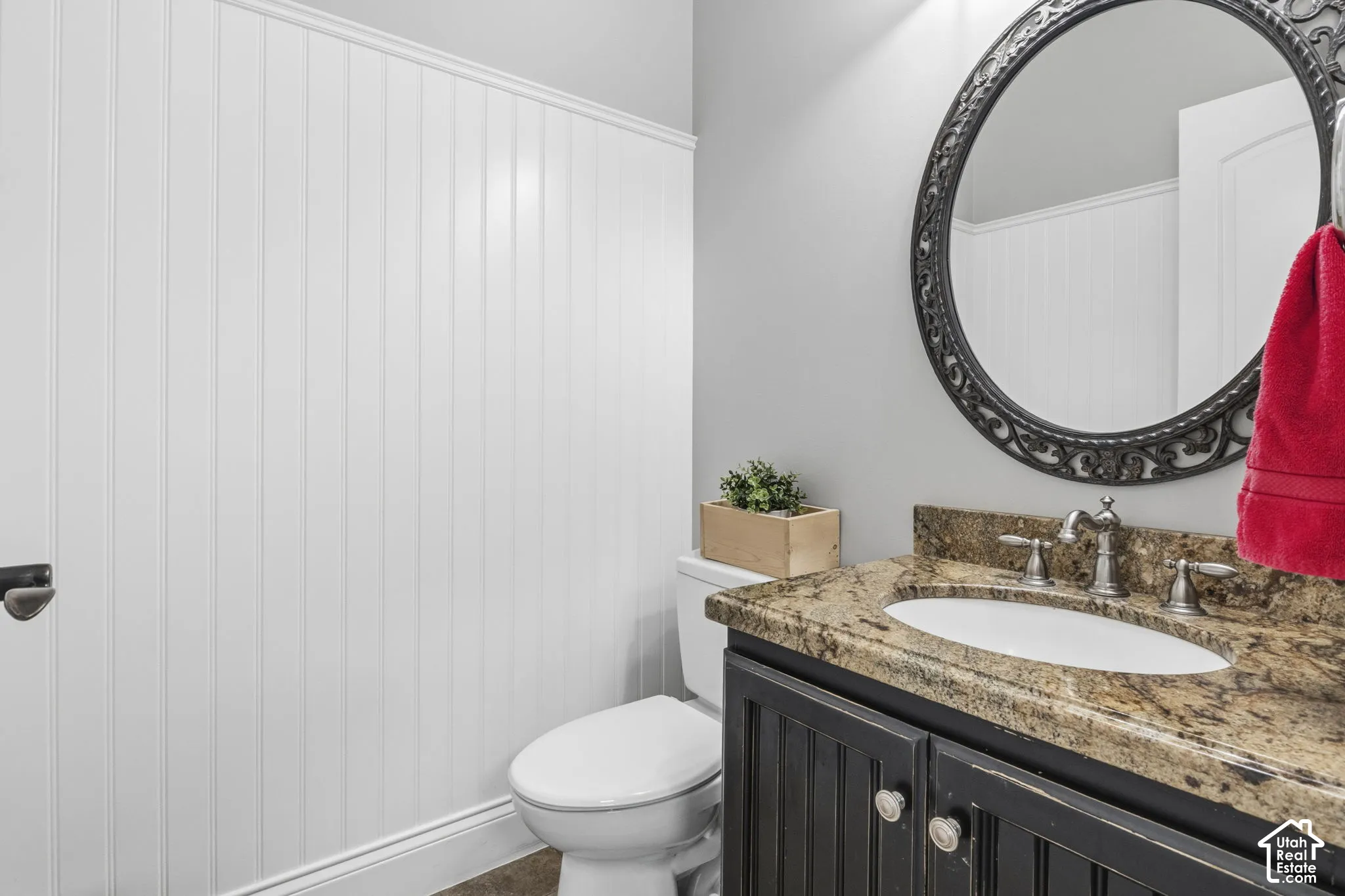 Bathroom featuring white vertical wall paneling, a dark-finish vanity with a stone-top counter, an undermount oval sink, and a decorative circular wall mirror