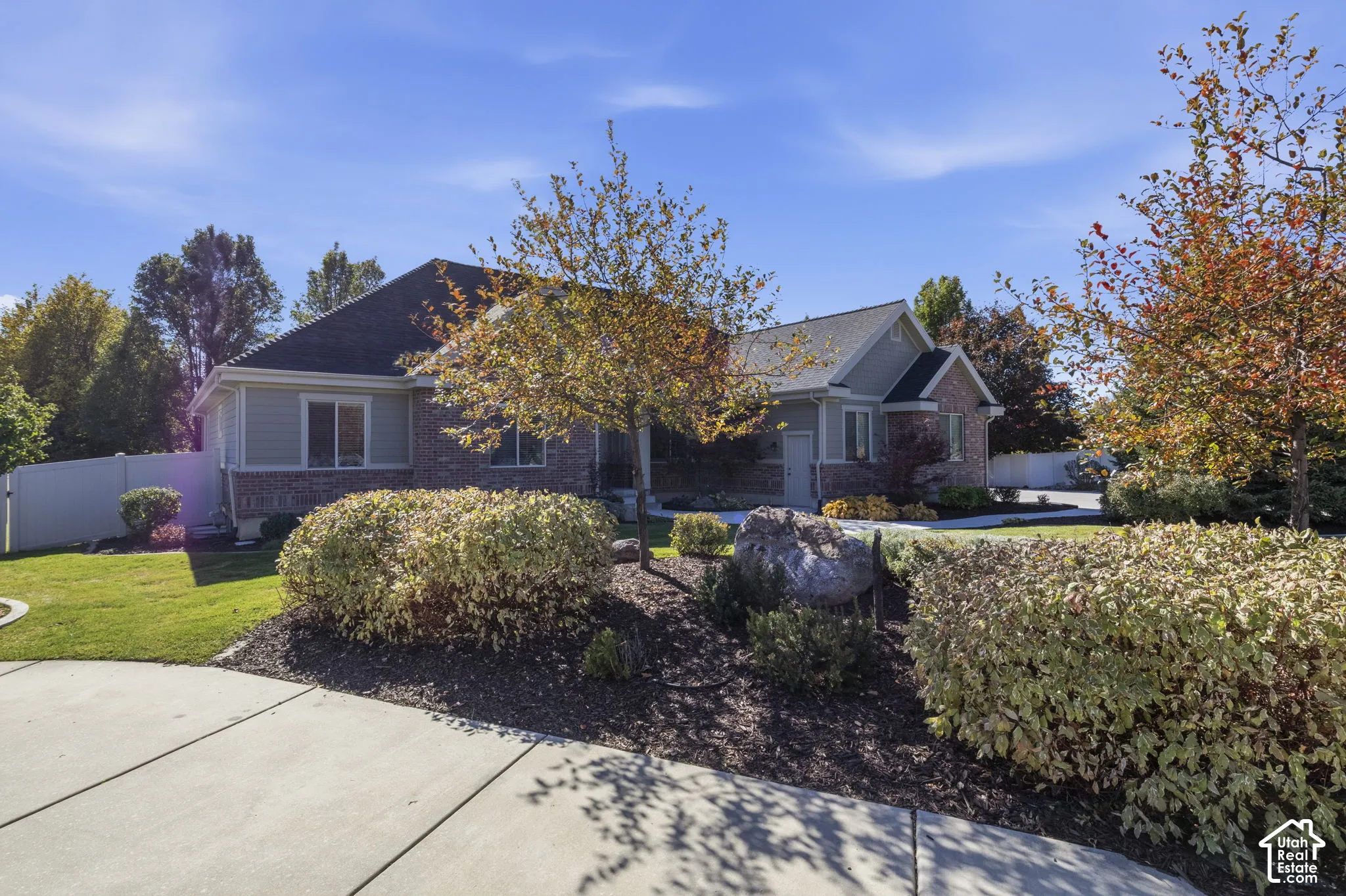 Single-story residence featuring brick and horizontal siding exterior, concrete driveway, and established landscaping with mature trees
