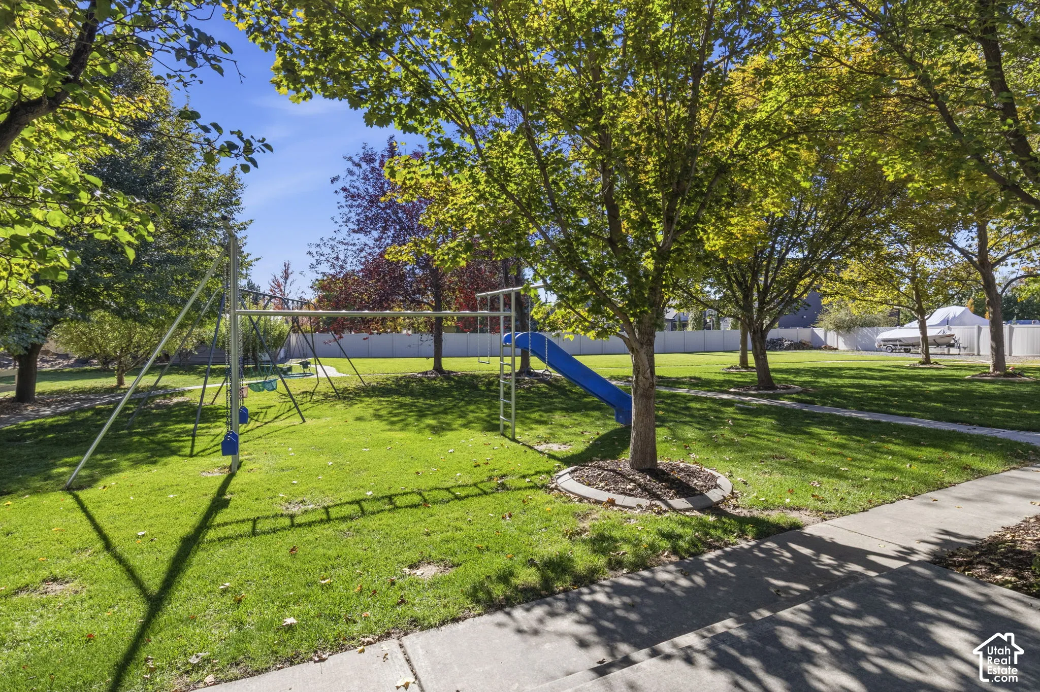 Expansive backyard featuring mature trees, manicured lawn, concrete walkways, and perimeter fencing