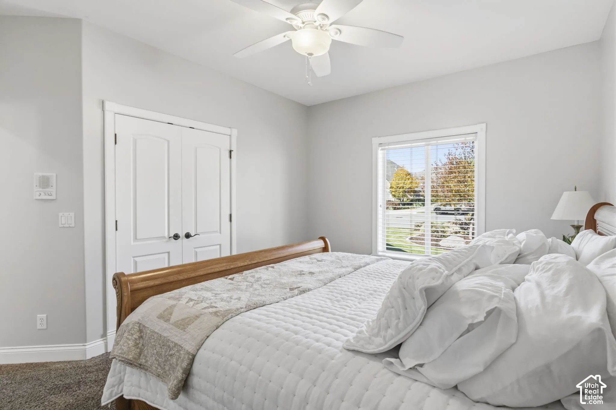 Neutral-toned room featuring a central ceiling fan with an integrated light fixture, double-door closet, and window with horizontal blinds