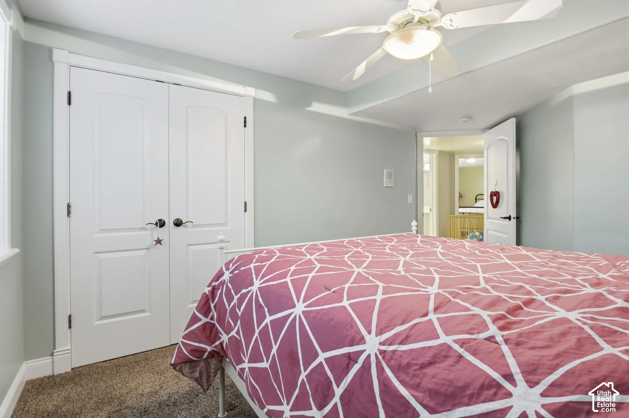 Room featuring neutral wall tones, wall-to-wall carpeting, white paneled double-door closet, and a ceiling-mounted light fixture with integrated fan