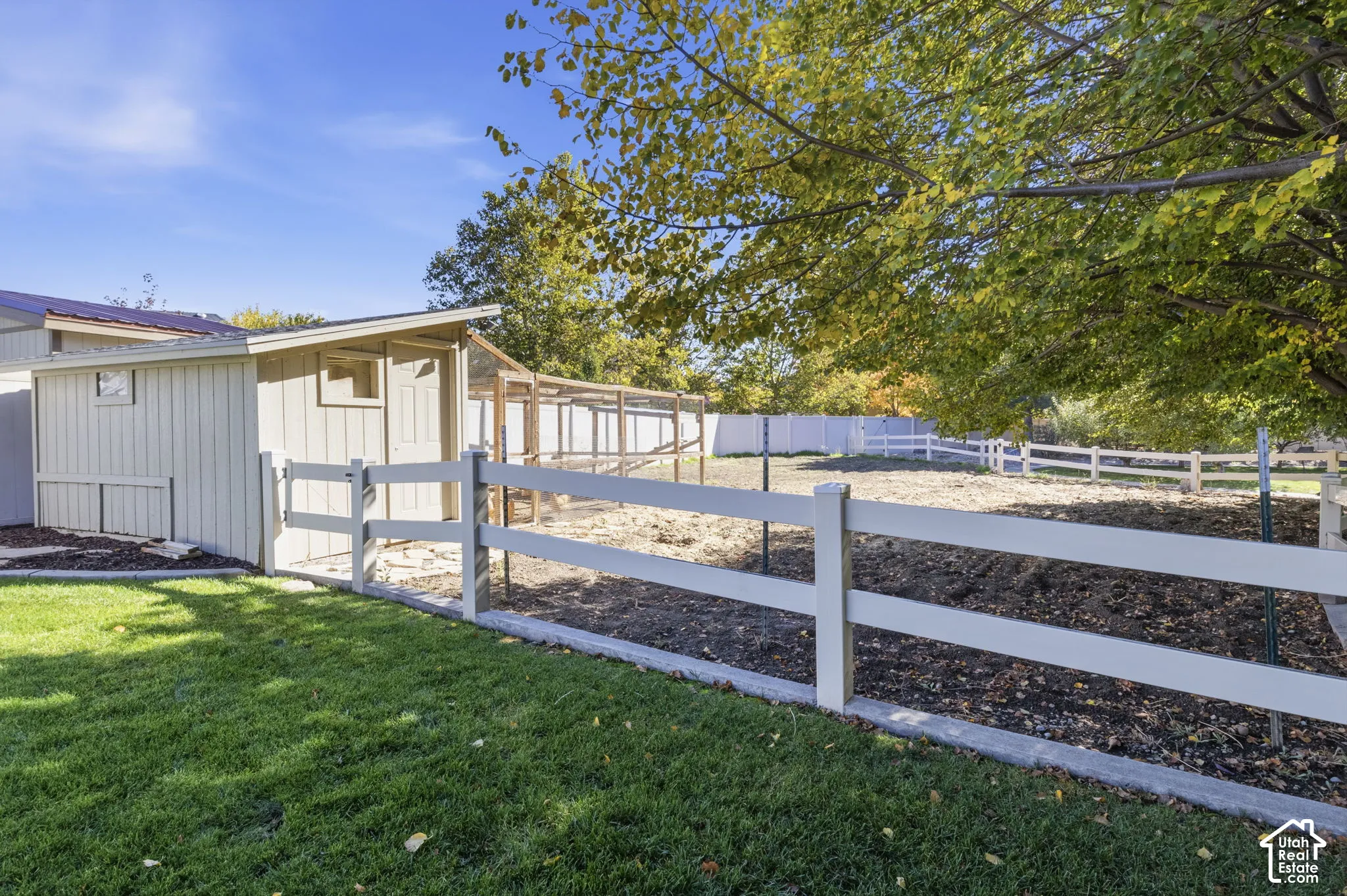 Fenced backyard featuring a storage shed, wood-post and rail fencing, and mature trees