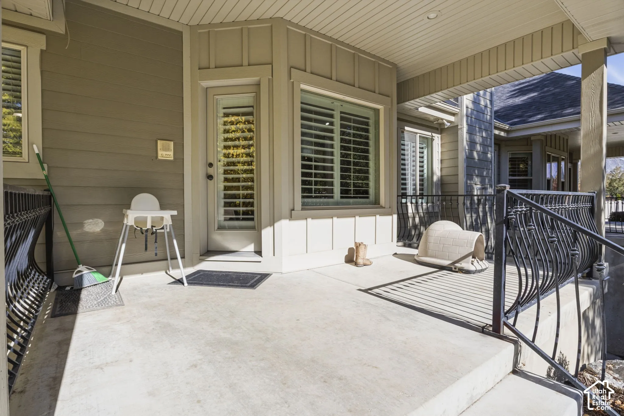 Covered concrete patio featuring board-and-batten siding, decorative metal railings, and dual-pane windows with integrated shutters