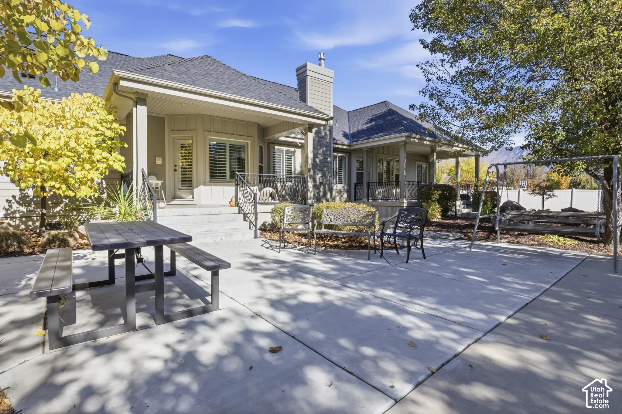 Exterior patio featuring concrete hardscaping, covered porch area, metal railings, and chimney structure