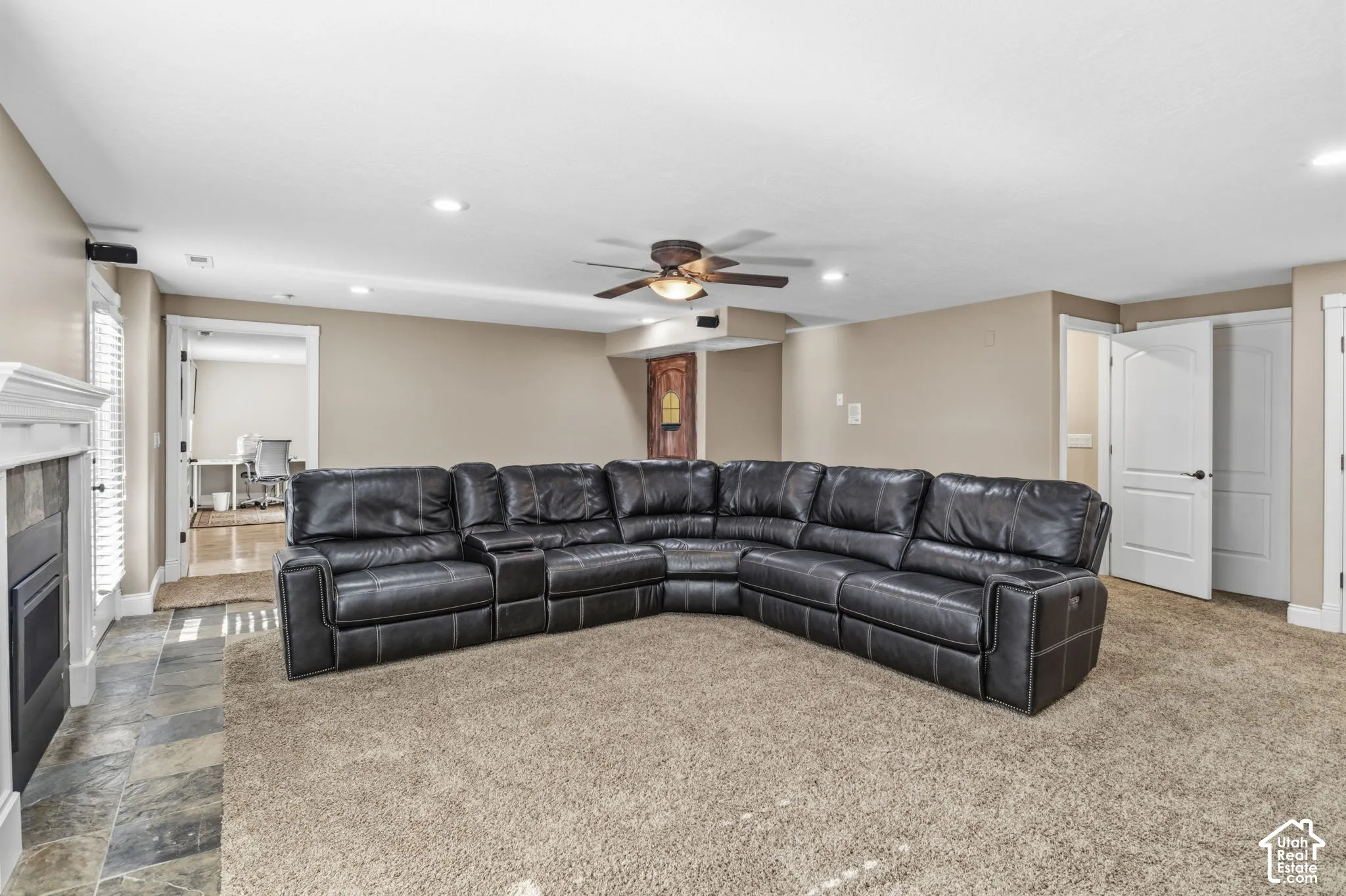 Fireplace with a stone-finish surround, recessed ceiling lighting, ceiling fan, and multi-panel doors