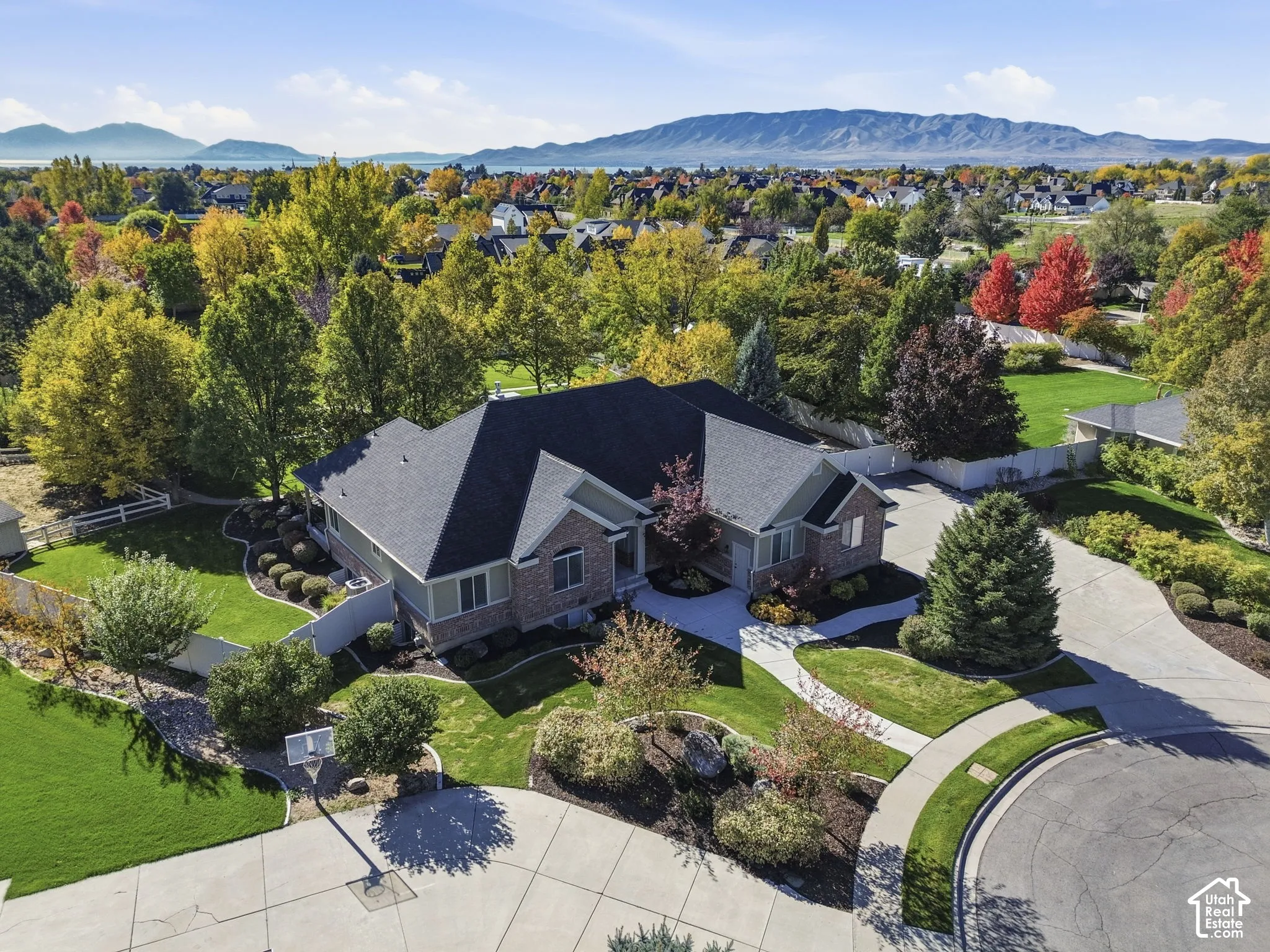 Single-story residence with a brick and siding exterior, multi-gabled roof, expansive landscaped grounds, concrete driveway, and mountain backdrop