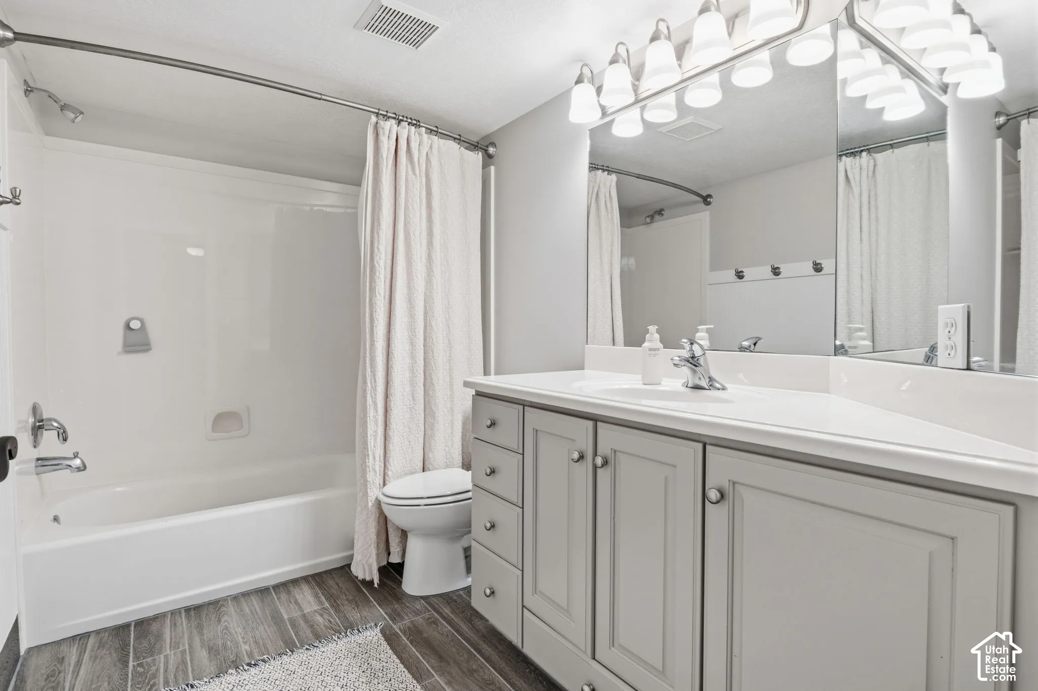 Bathroom featuring a vanity with shaker-style cabinetry, wood-finish flooring, a full-width mirror, a tub-shower combination, and a multi-light fixture