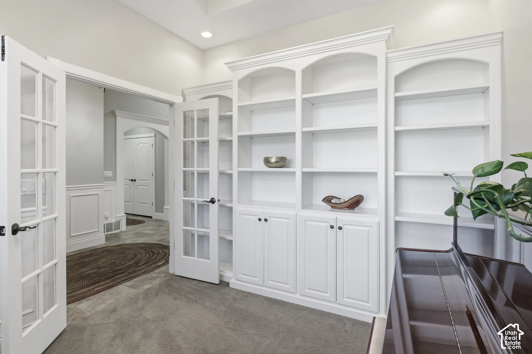 Custom floor-to-ceiling white built-in cabinetry featuring arched shelving and lower enclosed storage, paired with classic French doors and architectural millwork including wainscoting