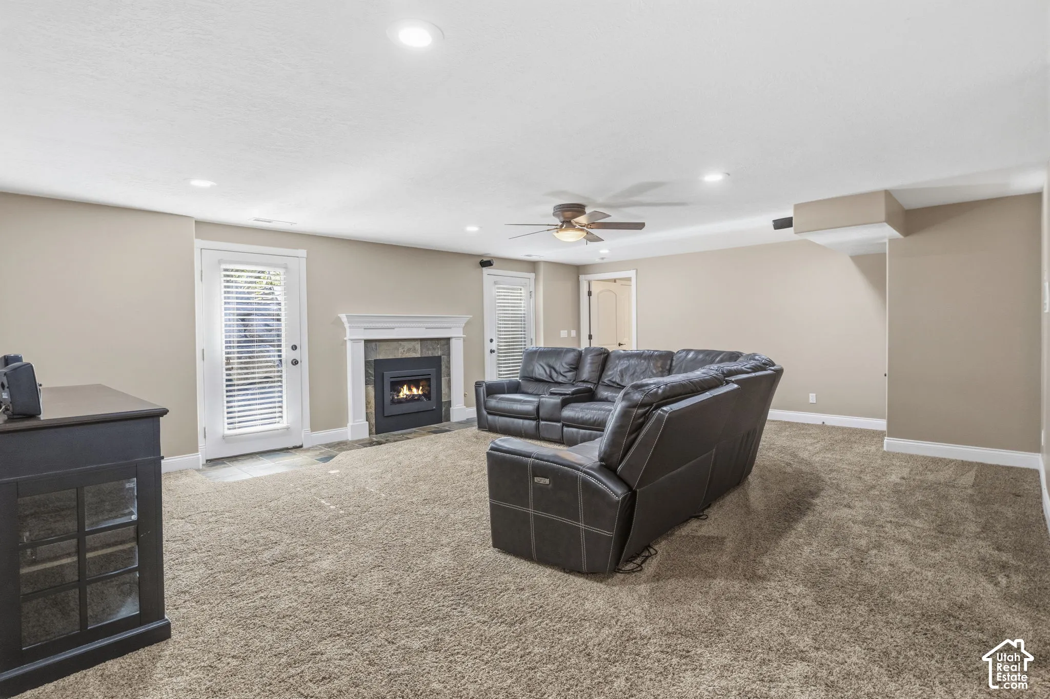 Fireplace featuring a stone tile surround and white mantel, two glass-paned exterior doors, recessed ceiling lighting, and a ceiling fan