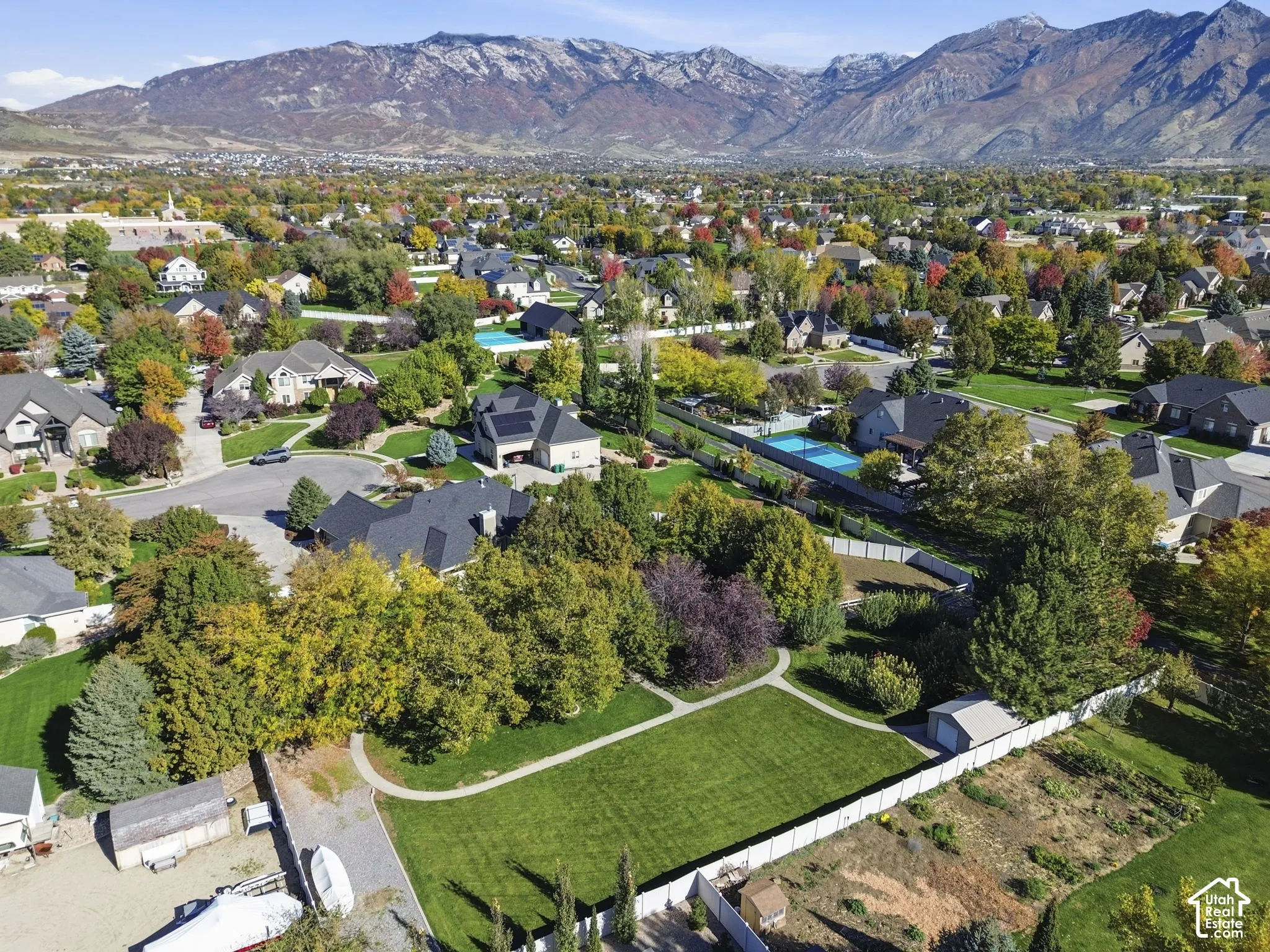 Aerial perspective showcasing expansive grounds with mature trees, manicured lawn, concrete walkways, a detached garage, and mountain backdrop