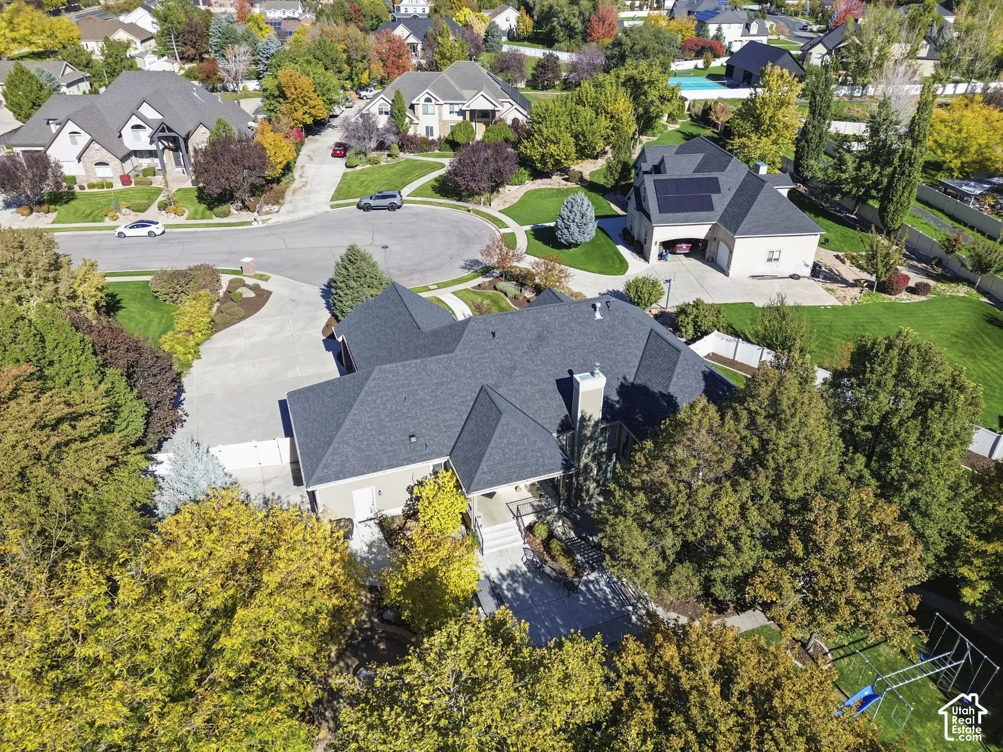 Aerial perspective featuring a multi-gabled roofline, concrete driveway, mature landscaping, and an expansive lawn