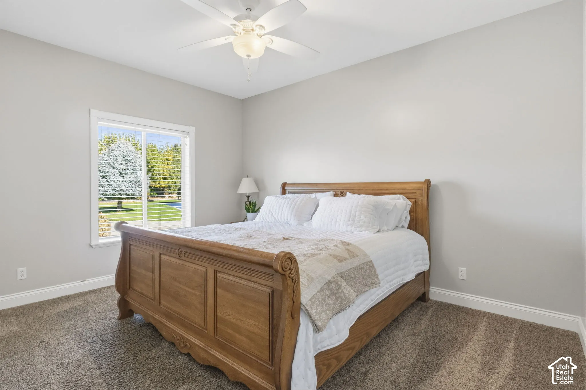 Neutral wall tones, carpeted flooring, sliding window with exterior greenery, and a white ceiling fan with integrated lighting