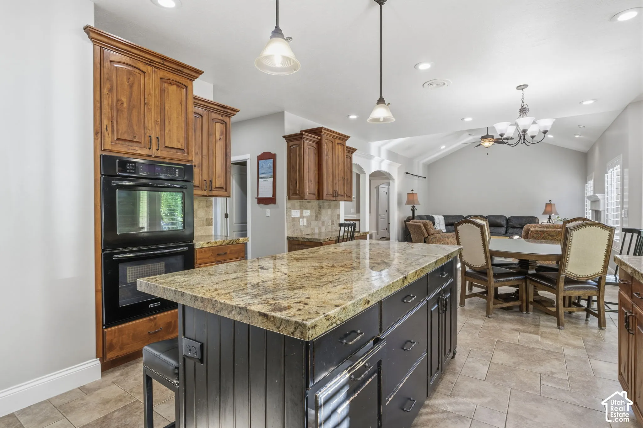 Kitchen featuring stone-topped center island with dark cabinetry, built-in double oven, wood-finish cabinetry, tile flooring, and vaulted ceiling