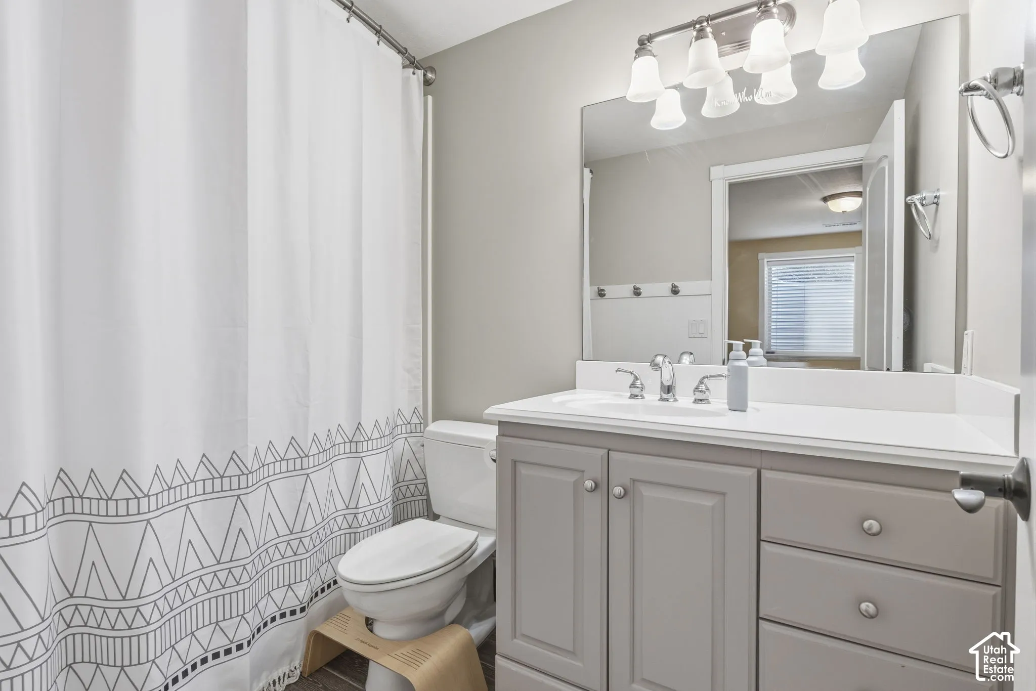 Bathroom featuring a vanity with shaker-style cabinetry, solid-surface countertop, integrated basin, oversized wall-mounted mirror, and multi-bulb vanity lighting