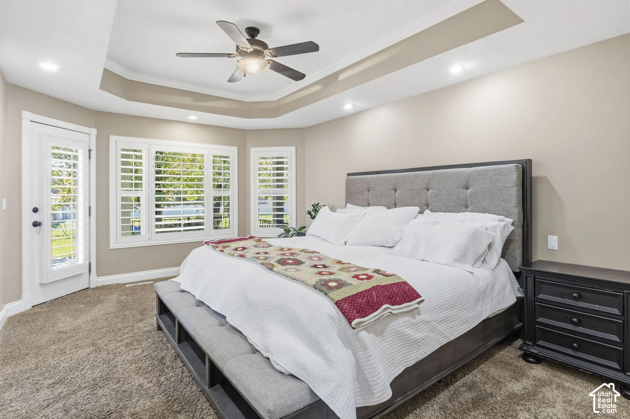 Tray ceiling with a central ceiling fan, recessed lighting, plantation shutters, and a glass-paneled exterior door