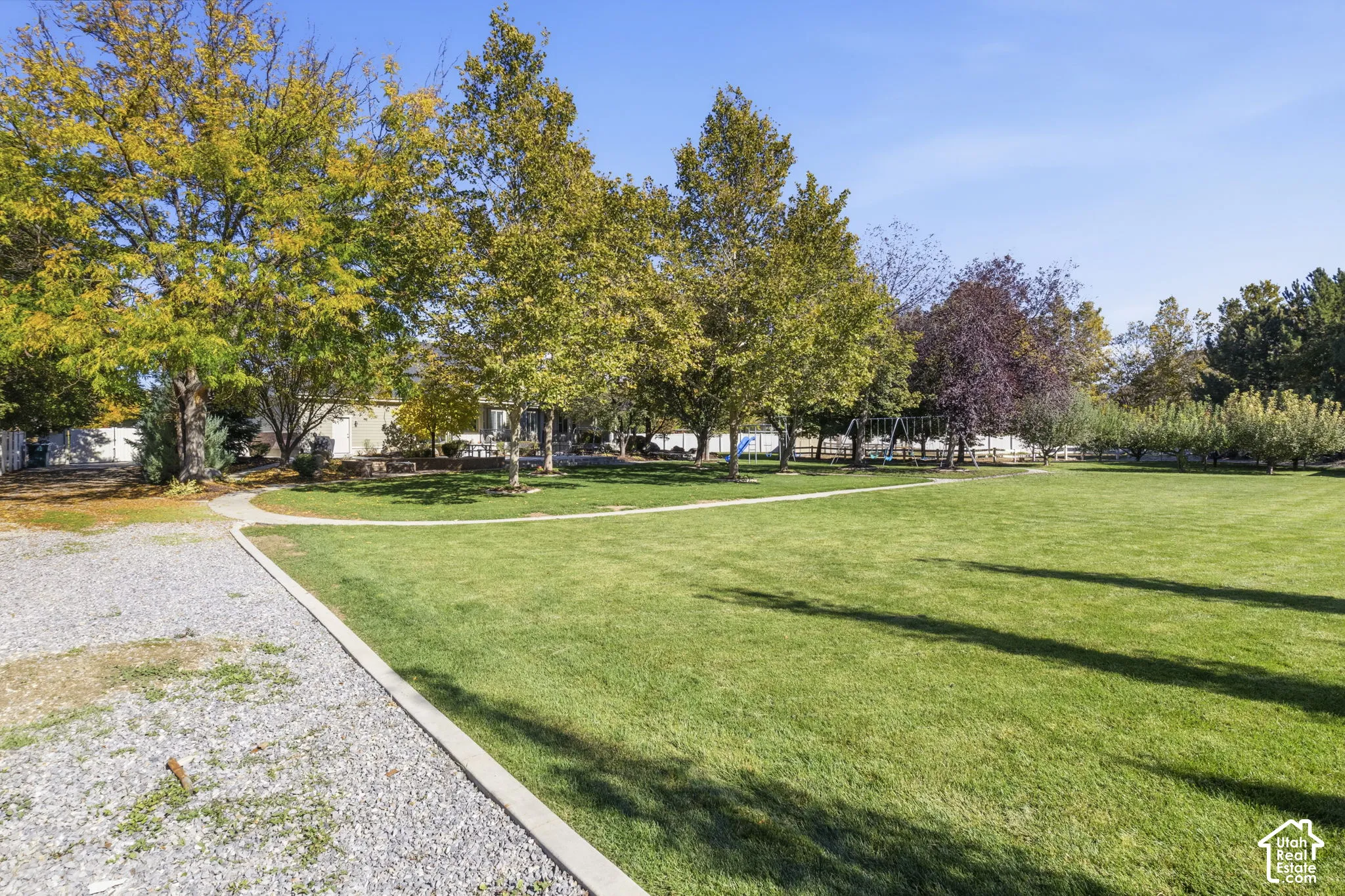 Expansive grounds featuring a manicured lawn, mature trees, concrete pathways, and gravel border