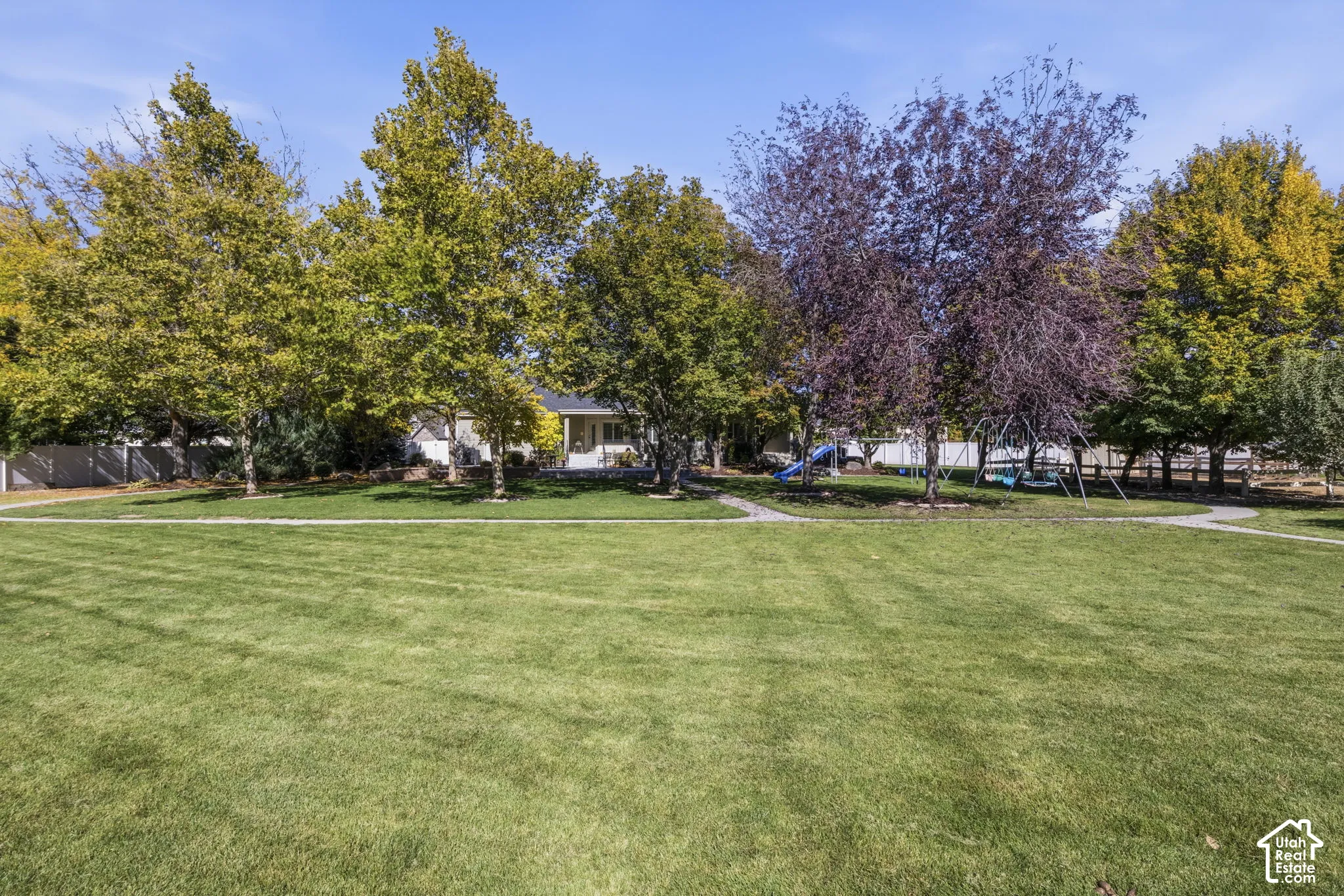 Expansive backyard featuring a manicured lawn, mature trees, stone pathway, and perimeter fencing