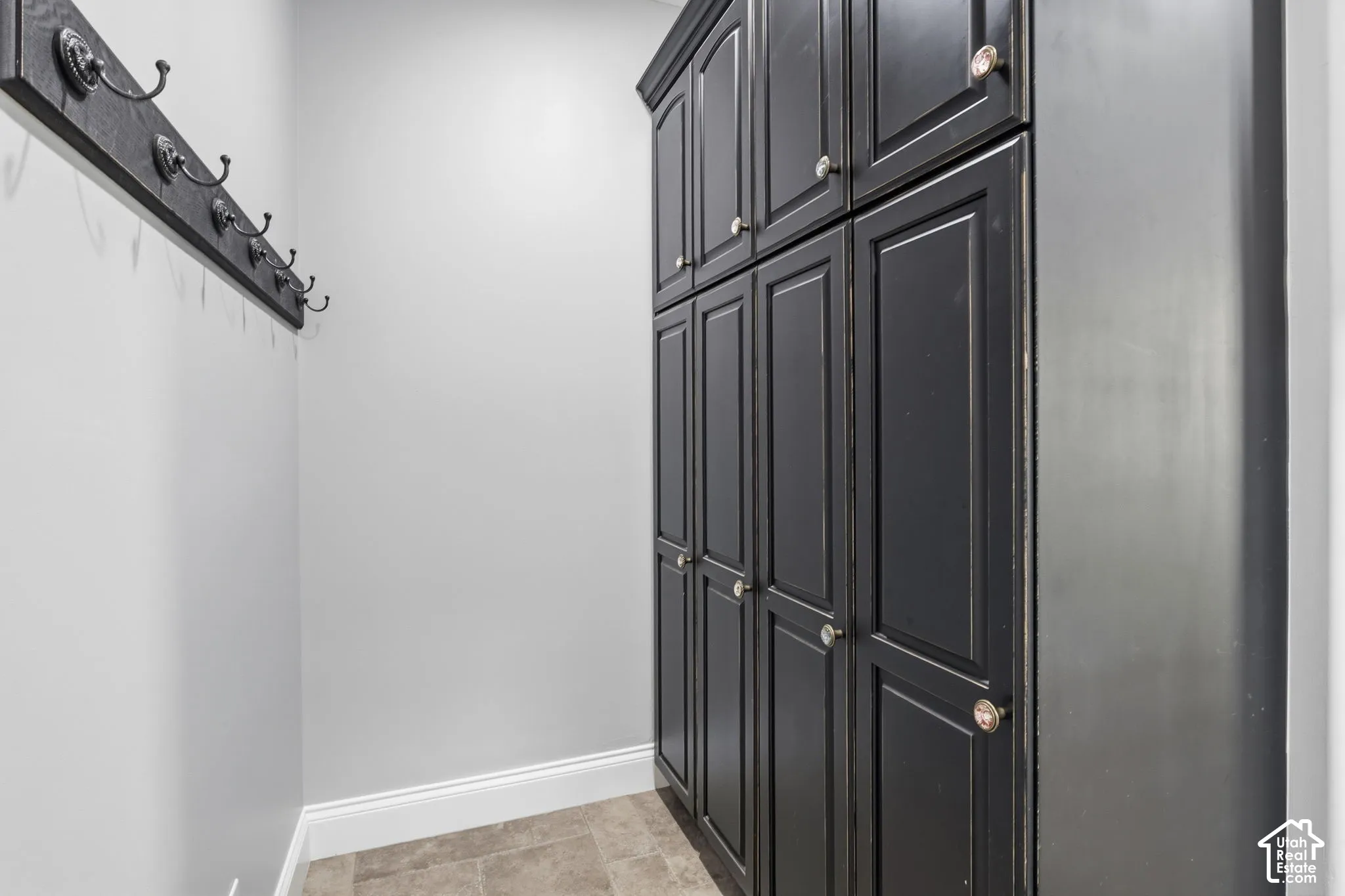 Floor-to-ceiling built-in cabinetry with black finish, raised panel doors, and silver-tone hardware, paired with a matching wall-mounted coat rack featuring multiple hooks and stone-composite tile flooring