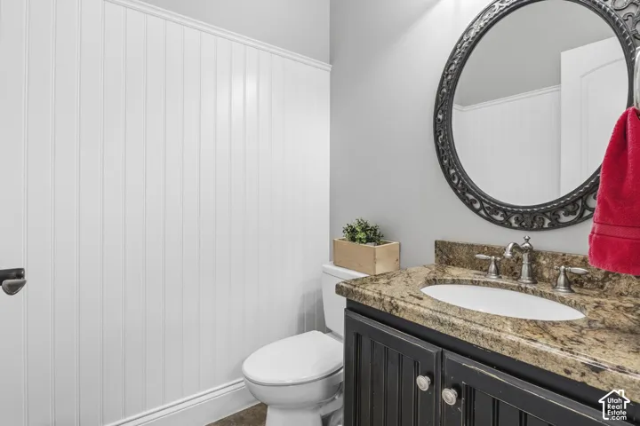Bathroom featuring white vertical wall paneling, a dark-finish vanity with a stone-top counter, an undermount oval sink, and a decorative circular wall mirror