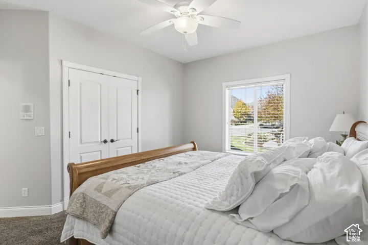 Neutral-toned room featuring a central ceiling fan with an integrated light fixture, double-door closet, and window with horizontal blinds