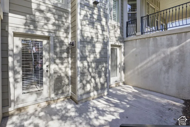 Exterior patio space featuring horizontal siding, concrete foundation, two glass-panel exterior doors, and a raised balcony with black metal railings
