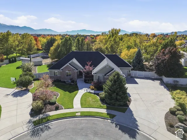 Single-story residence featuring brick and siding exterior, expansive concrete driveway, manicured lawn, and mountain backdrop