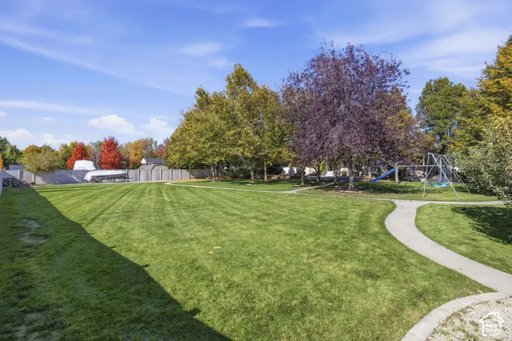 Expansive backyard featuring a manicured lawn, concrete pathways, mature trees, and perimeter fencing