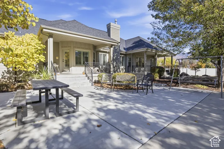 Exterior patio featuring concrete hardscaping, covered porch area, metal railings, and chimney structure