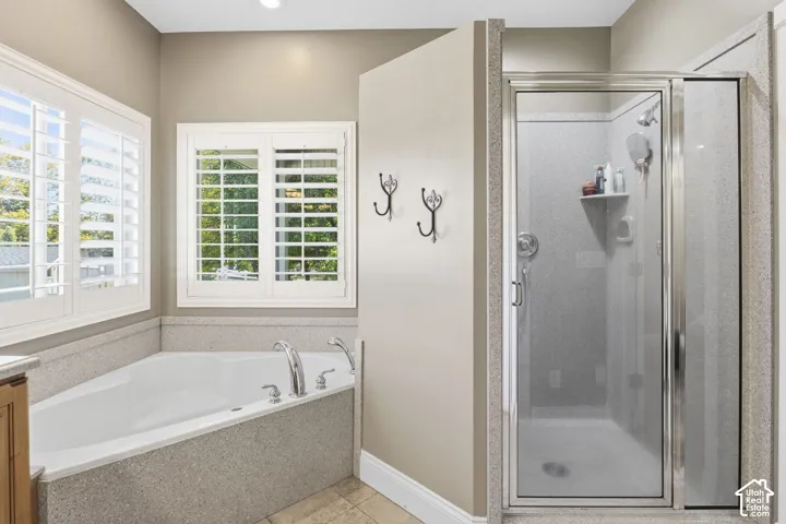 Corner soaking tub and separate shower enclosure with stone-finish surrounds, windows featuring plantation shutters, and mounted wall hooks