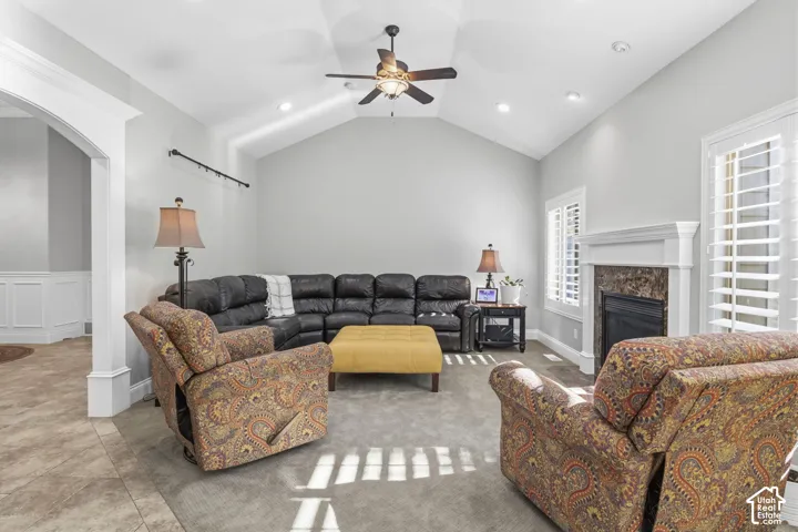 Vaulted ceiling featuring a central lighted ceiling fan, recessed lighting, a stone-surround fireplace with a classic mantel, and white plantation shutters
