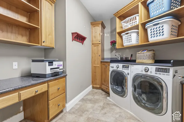 Laundry space featuring natural wood cabinetry, integrated shelving, dark stone-finish countertops, and a stainless steel utility sink