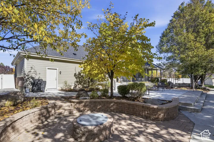 Backyard featuring a tiered paver stone patio, built-in circular masonry fire pit, retaining wall, concrete hardscaping, and mature trees
