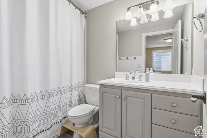 Bathroom featuring a vanity with shaker-style cabinetry, solid-surface countertop, integrated basin, oversized wall-mounted mirror, and multi-bulb vanity lighting