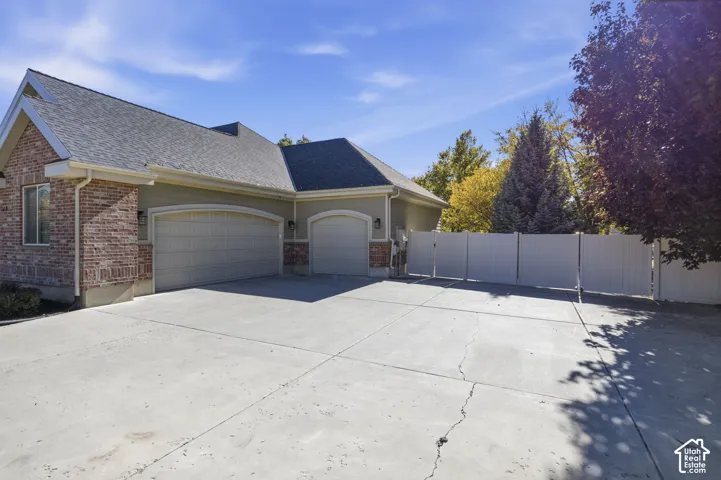 Exterior featuring brick and horizontal siding, a three-car garage with arched doors, a concrete driveway, and a white privacy fence