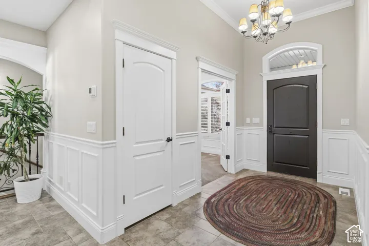 Foyer featuring a dark-toned entry door with an arched transom window, wainscoting, tile flooring, and a multi-light chandelier