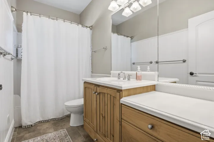 Bathroom featuring a wood-finish vanity with a light-toned countertop, beadboard wainscoting, a large plate-glass mirror, and multi-bulb overhead lighting