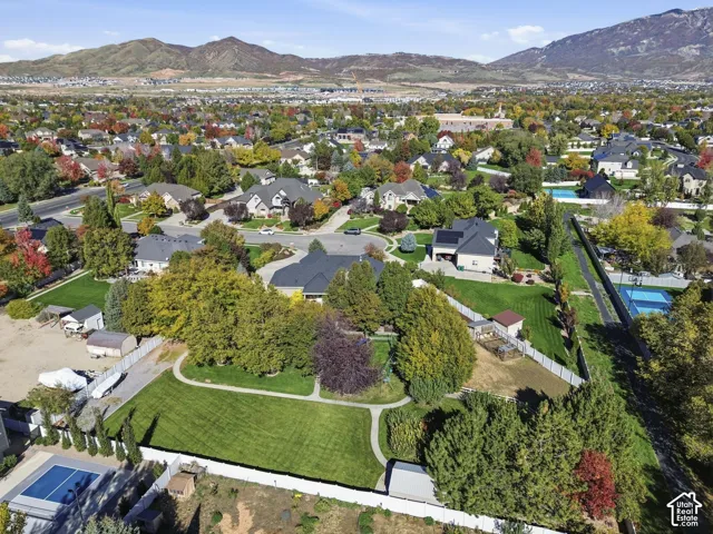 Aerial perspective featuring expansive manicured lawns, mature shade trees, white vinyl perimeter fencing, and mountain scenery
