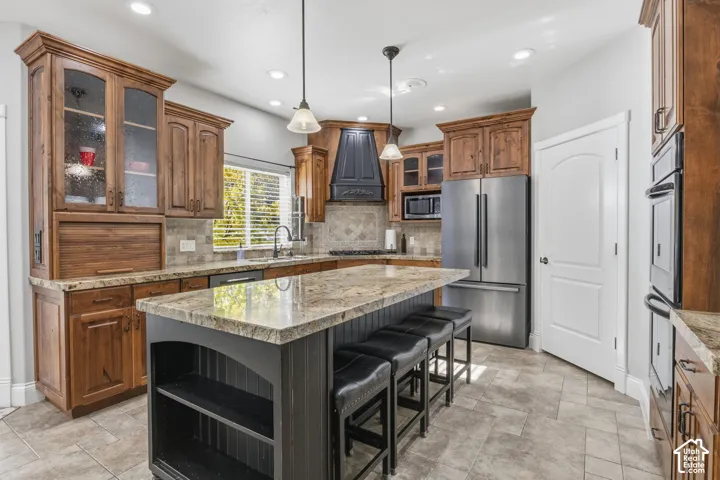 Kitchen featuring stained wood cabinetry, stone countertops, a center island with integrated shelving, stainless steel appliances, and tile flooring