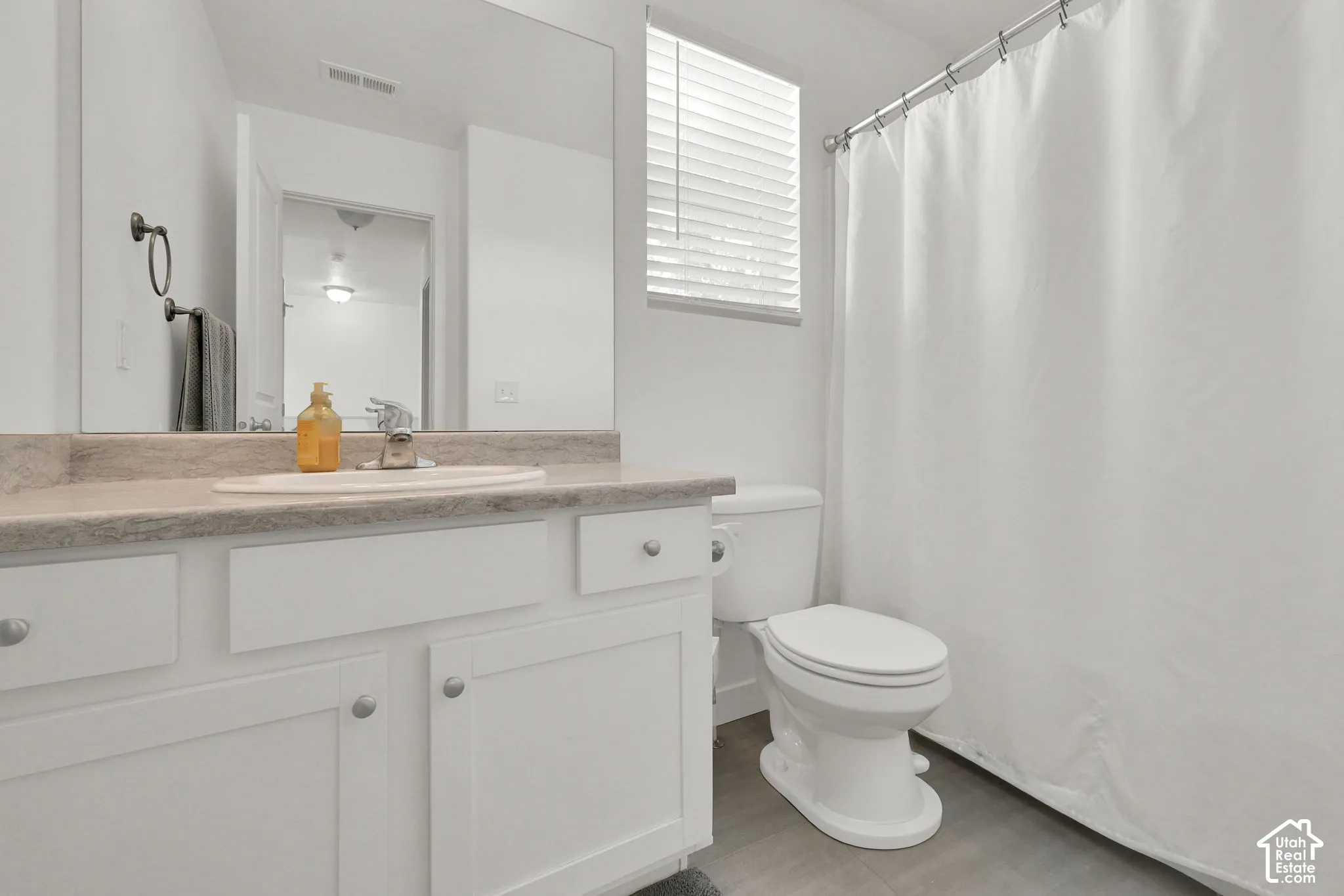 Bathroom featuring a white vanity with integrated oval sink, stone-finish countertop, large wall-mounted mirror, and combination shower and tub with horizontal slat blinds