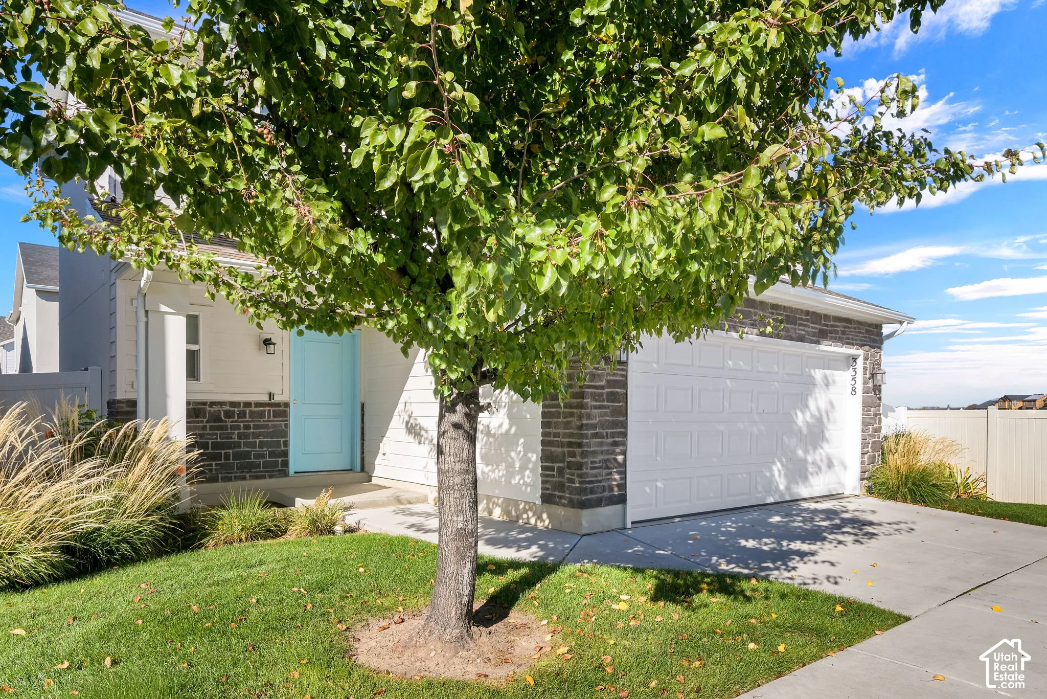 Exterior featuring stone veneer siding, double-car garage, white vinyl fencing, and a concrete driveway