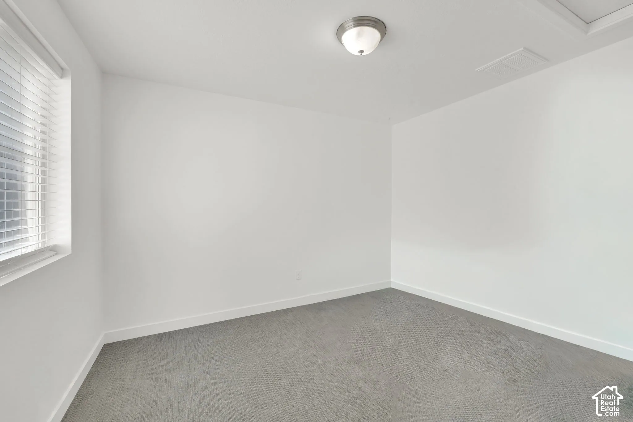 Neutral-toned interior space featuring wall-to-wall carpeting, white walls, and a ceiling-mounted flush-mount light fixture