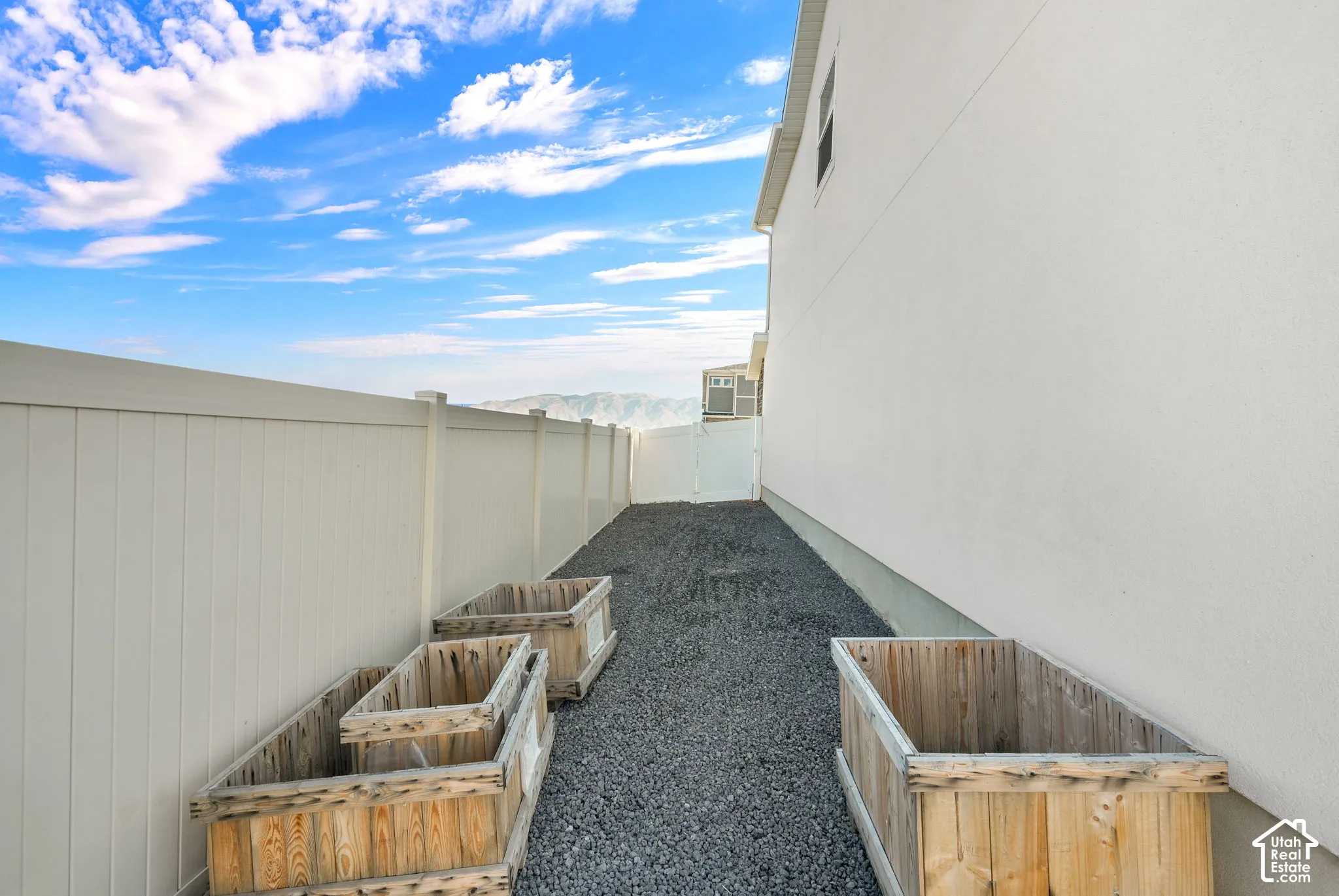 Side yard featuring gravel ground cover, white vinyl fencing, and built-in wood-finish planter boxes