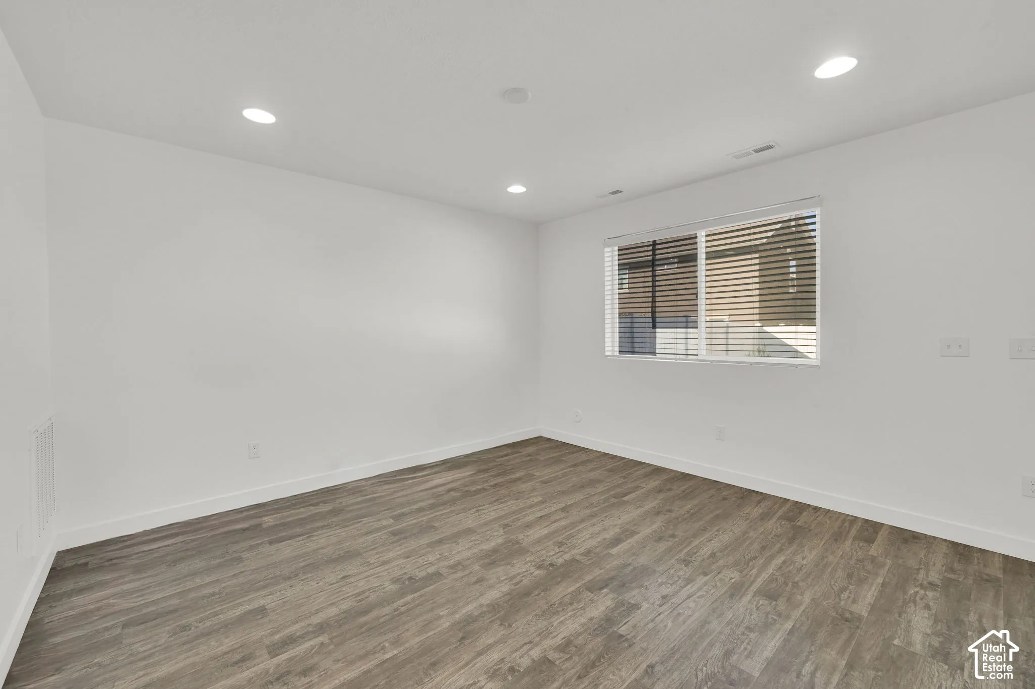Neutral-toned interior space featuring wood-finish flooring, recessed lighting, and a window with horizontal blinds